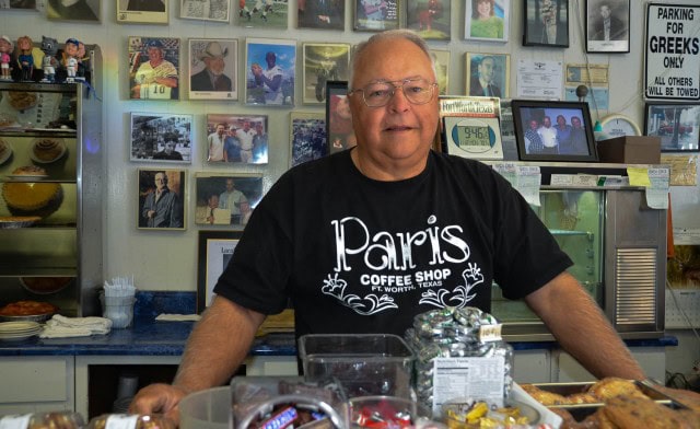 Mike Smith, owner of Paris Coffee Shop, in Fort Worth, Texas. Mike Smith, owner of Paris Coffee Shop, posing with collection of memorabilia displayed on wall and on shelves.