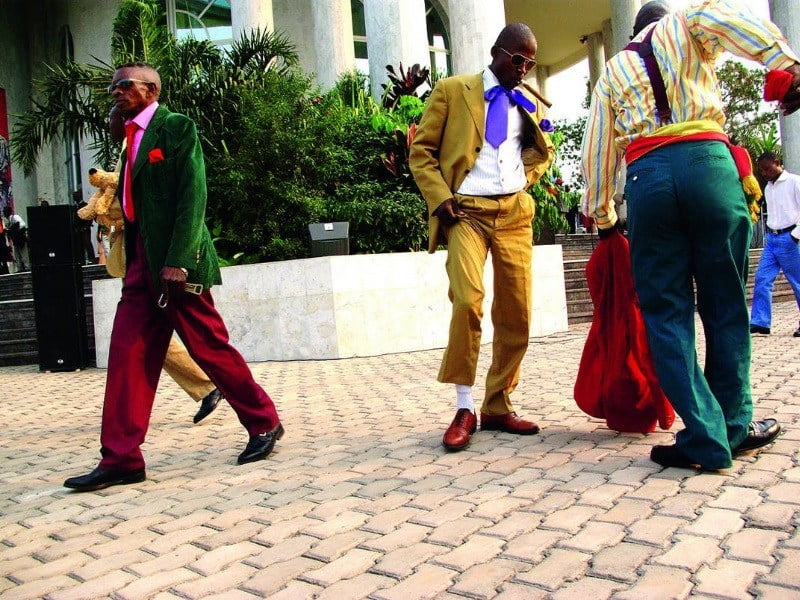 Os “sapeurs” são homens que desfilam nas principais avenidas da República Democrática do Congo Brazzaville e Kinshasa com fatos ocidentais elegantes, acrescentados de um charuto ou do tradicional cachimbo na boca. (Foto: Reprodução/MozLife BETA)