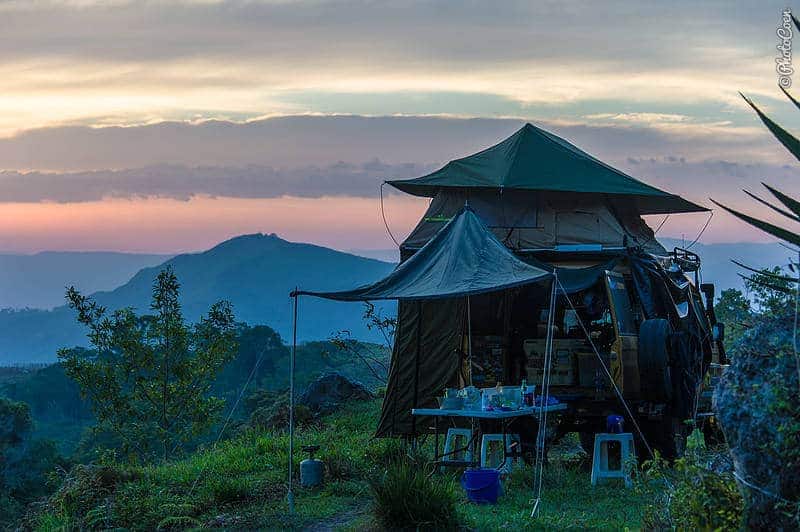 A car with a rooftop tent set in a landscape of mountains and grass.