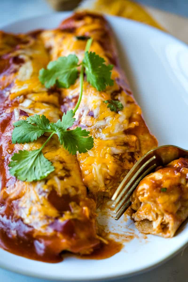 a fork cutting into chicken enchiladas on a plate