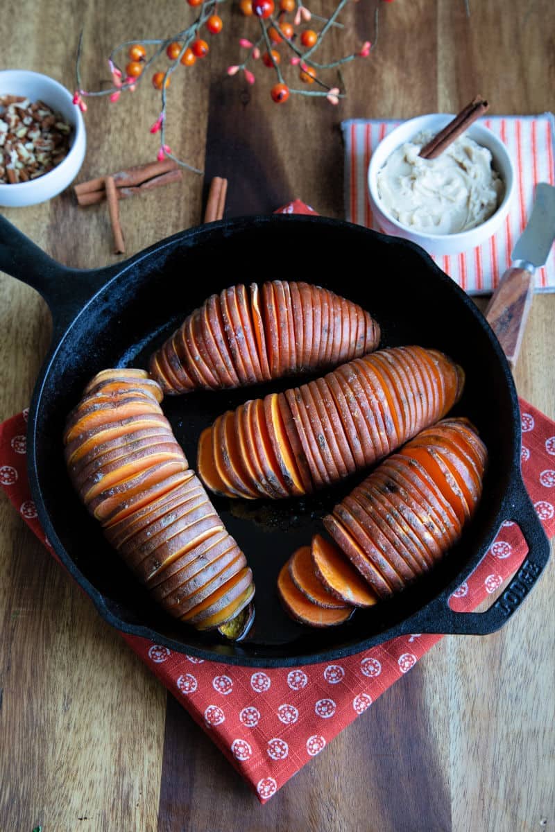 sweet potatoes in a cast iron skillet on wooden table with a bowl of cinnamon butter