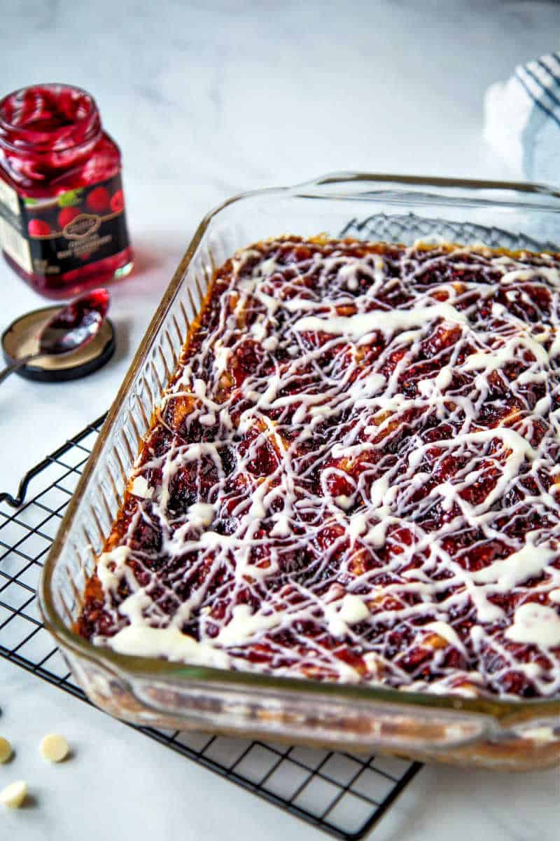 raspberry oatmeal bars in glass baking dish with an open jar of raspberry jam on the table