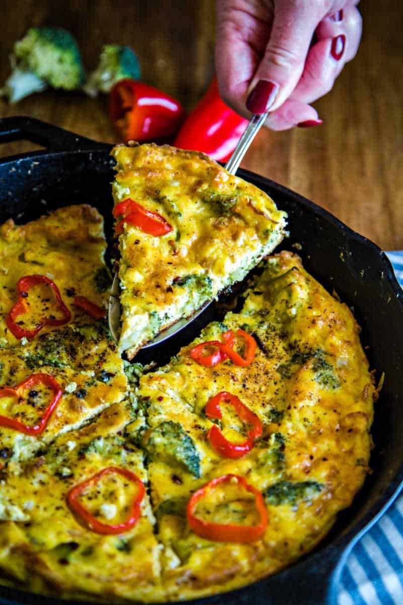 lifting a slice of broccoli frittata out of a cast iron skillet