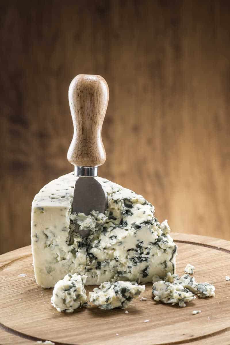 a wedge of blue cheese on a cheese board