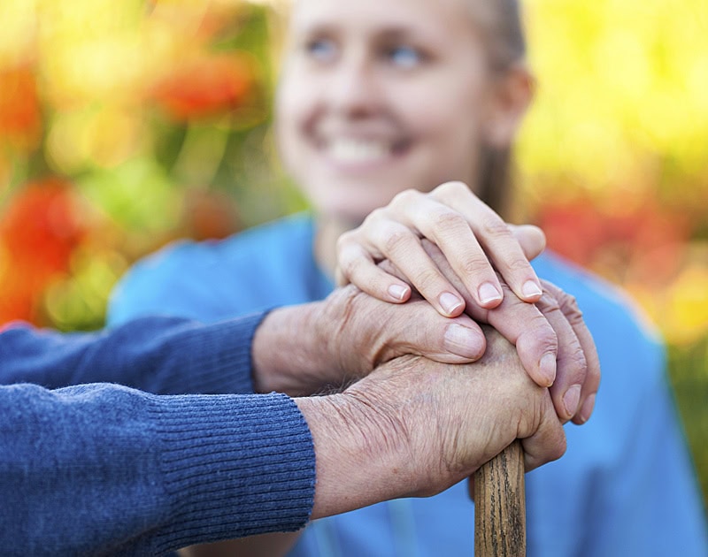 Caregiver with her hadns on top of elderly man's hands