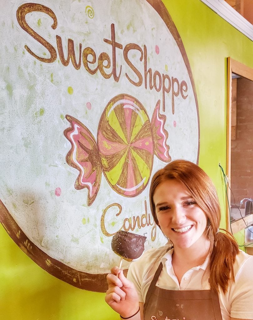 Young woman holding candy apple in front of green wall and sign