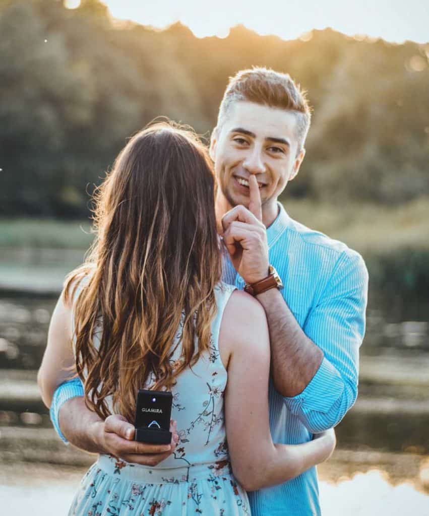 Man showing engagement ring to camera whilst hiding it behind partners back