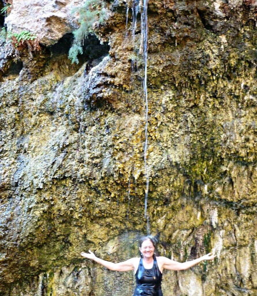 A stream of hot springs water showers Stacey standing below the cliff face.