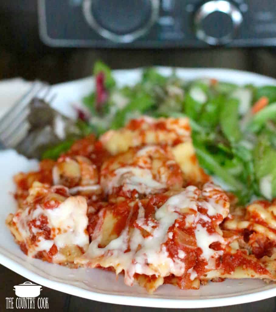 cooked ravioli, homemade marinara sauce, melted mozzarella cheese, on a white plate with a green salad and a Ninja slow cooker