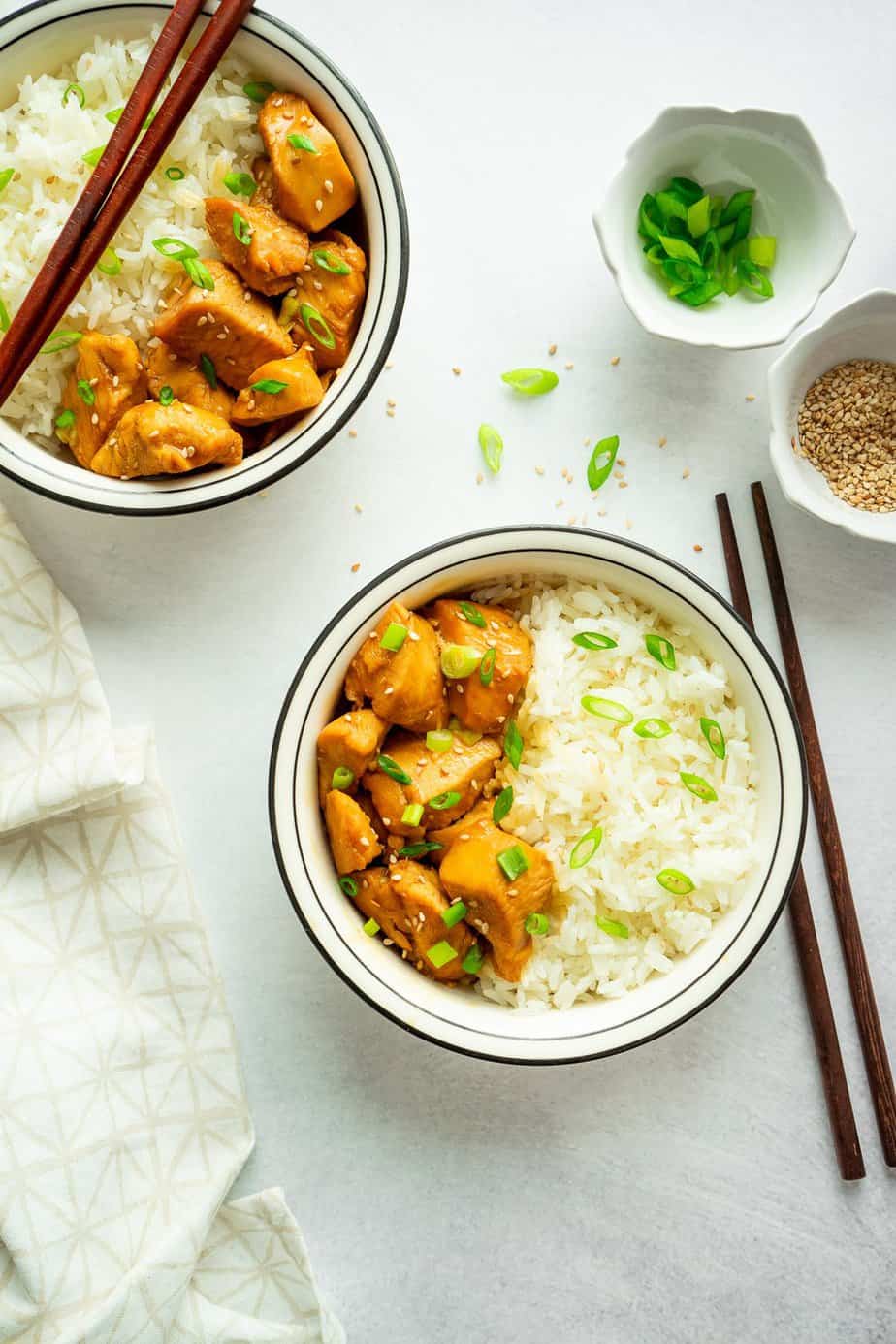 chopstick, chopped green onion in a small bowl, two serving of asian flavor chicken with white rice.