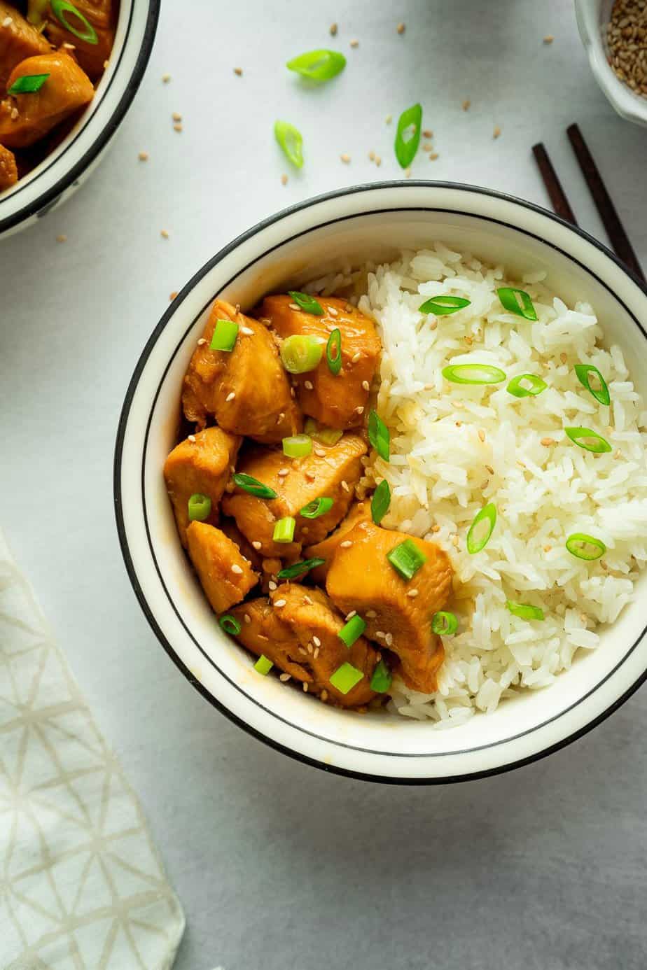 two bowls with white rice, pressure cooker chicken teriyaki with sesame seeds and green onion sprinkle over the rice and chicken pieces.