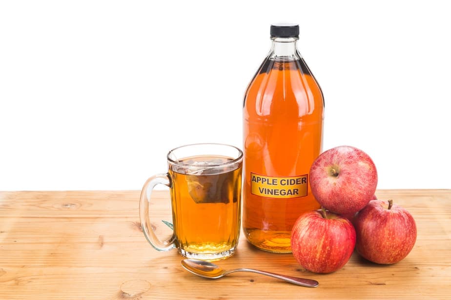 A spoon, a bottle, and a glass of apple cider vinegar with tree apples