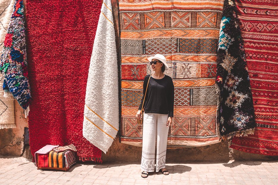 15 Important Things To Know Before You Travel To Morocco 2 L Jasmine stands in front of colourful woven rugs in Marrakech medina, Morocco
