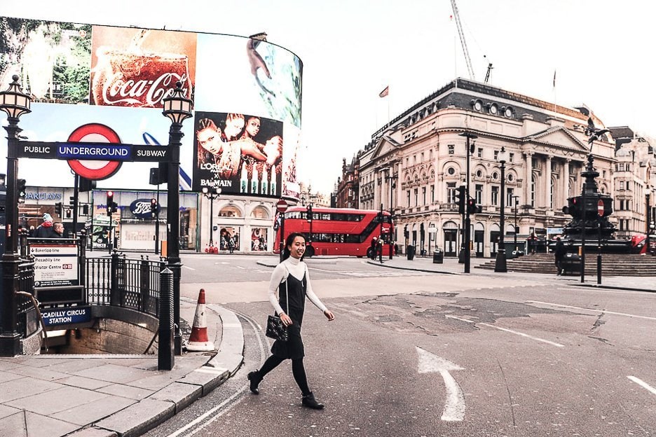 Why You Should Be An Expat At Least Once In Your Life 7 L Jasmine of The Travel Quandary walks through Piccadilly Circus on a winter's day. The TV screens and a red double decker bus is in the background. London - United Kingdom