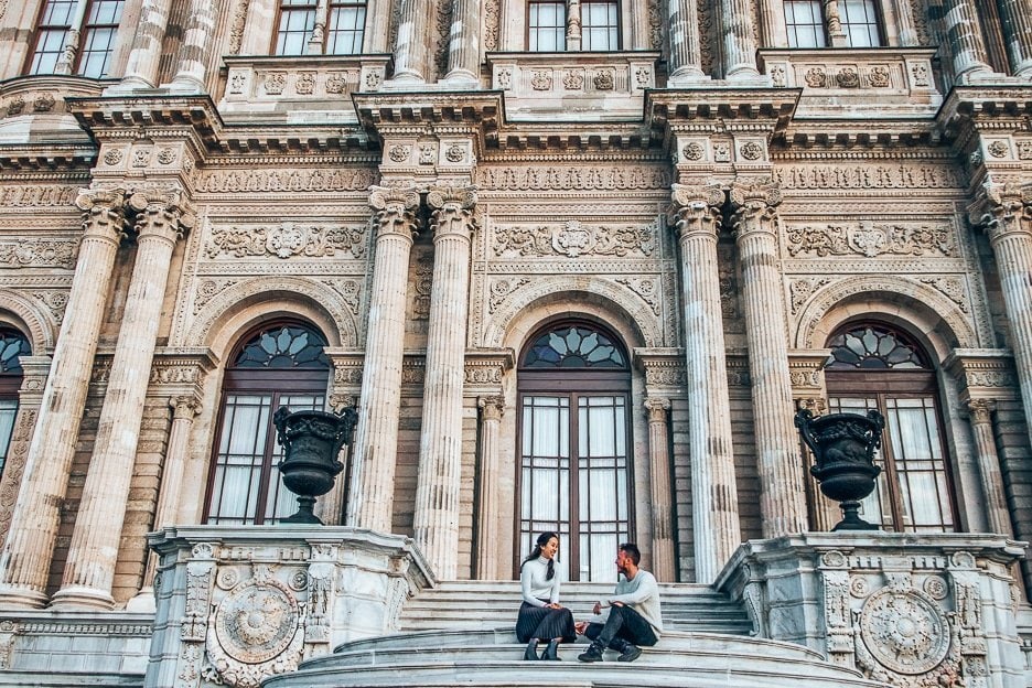About Us 1 L A couple sit on the stairs smiling at each other in front of Dolmabahce Palace in Istanbul, Turkey