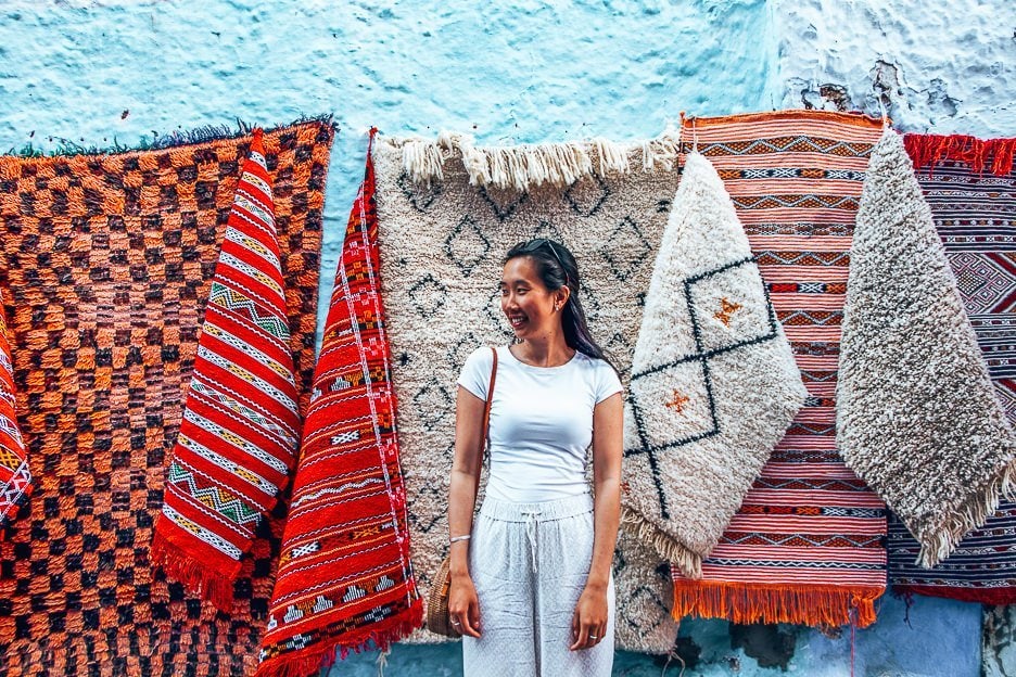 The Perfect Itinerary For 2 Days In Chefchaouen 10 L A woman wearing white stands in front of colourful woven rugs in Chefchaouen, Morocco