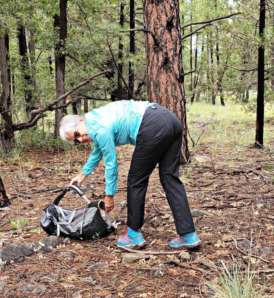 Unstoppable Stacey bends over to pick up pack demonstrating stretch of KÜHL rain pants