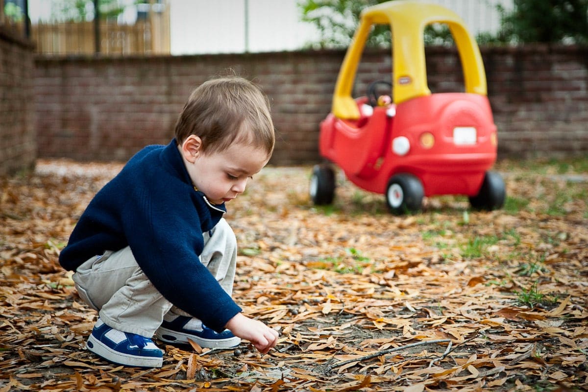 Image of baby boy crouching down to touch leaves on the ground in a playground.