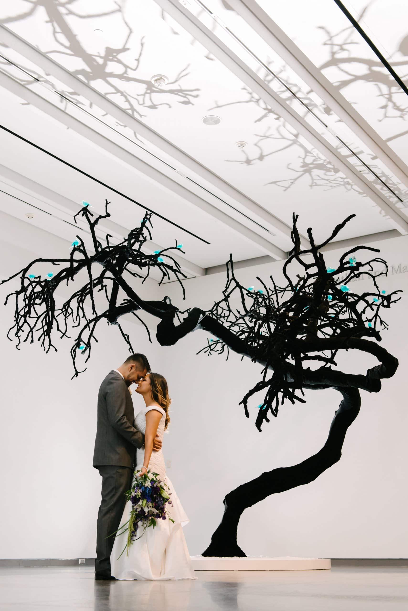 JavierAnita-82 Phoenix Art Musuem wedding couple standing in front of black tree indoors part of art exhibit