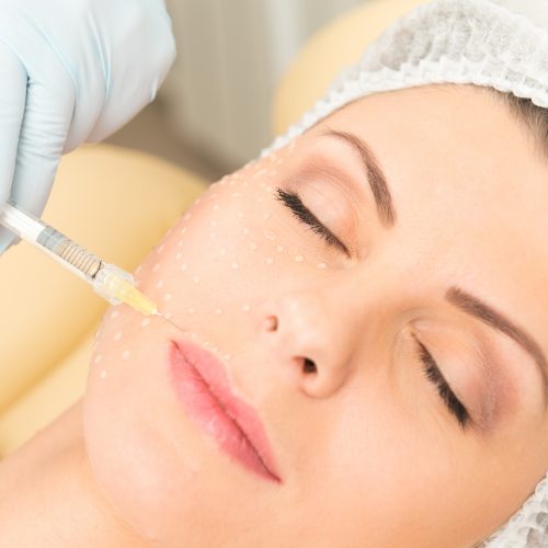 Cosmetic injection to the pretty caucasian woman face and beautician hands with syringe