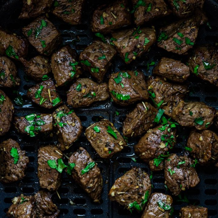 Air fryer steak bites inside the basket and garnish with parsley.