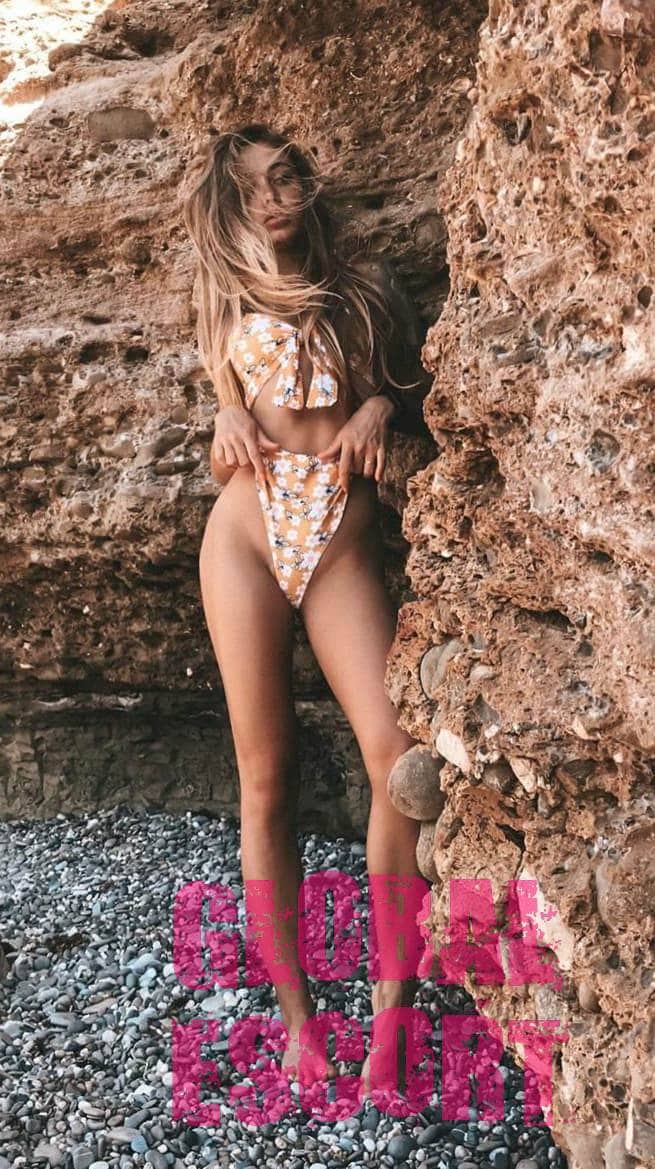 sexy brown-haired escort in a gold bathing suit on the beach at a photo shoot