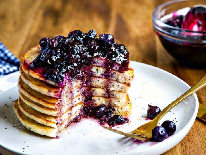 Stack of Lemon Poppy Seed Pancakes with Blueberry Compote on a white plate with fork