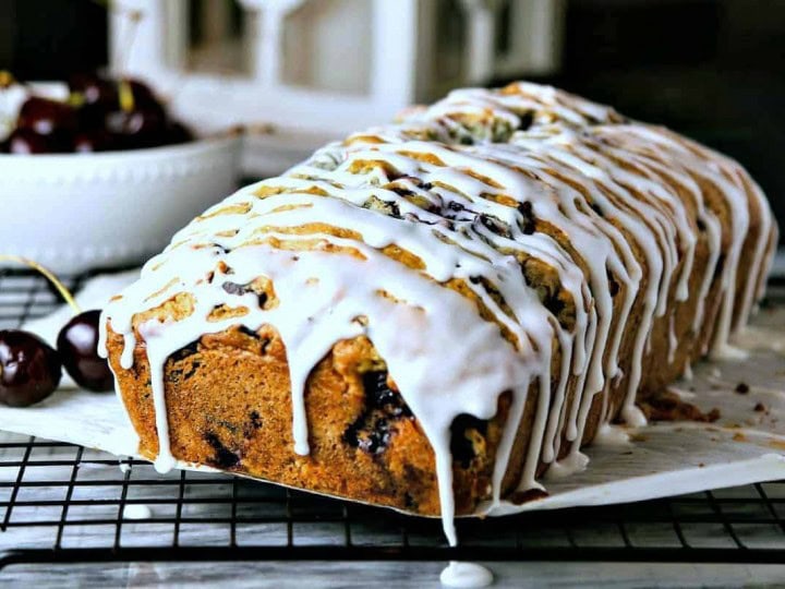A loaf of cherry chocolate chunk bread with a powdered sugar glaze dripping off the sides
