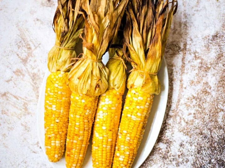 grilled corn in husk on a white platter