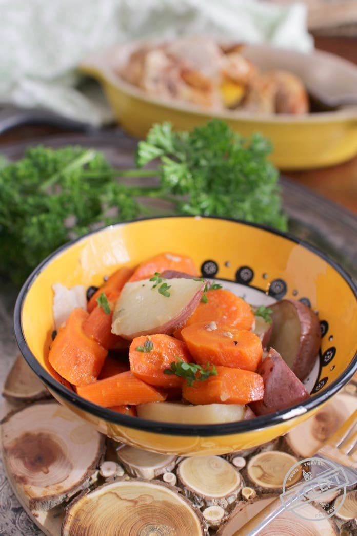 Roasted sliced red potatoes and carrots in a small bowl on a wooden trivet with a fork