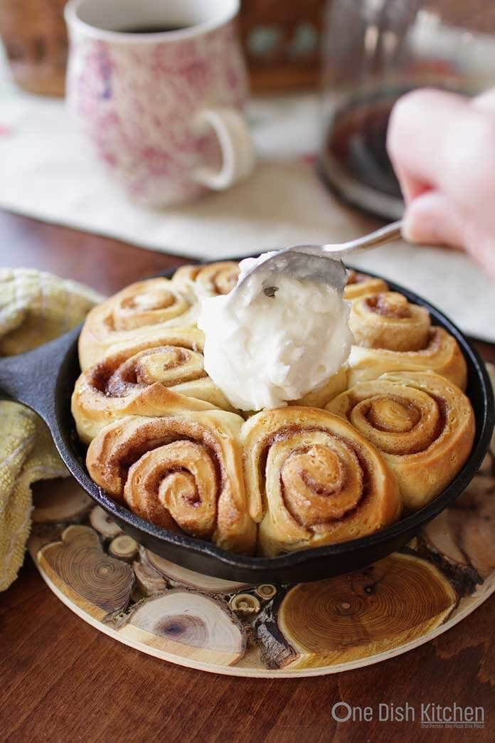 Spreading frosting over the cinnamon rolls | One Dish Kitchen