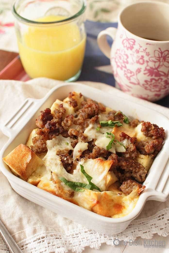 Breakfast casserole in a small baking dish next to a glass of orange juice and a coffee mug