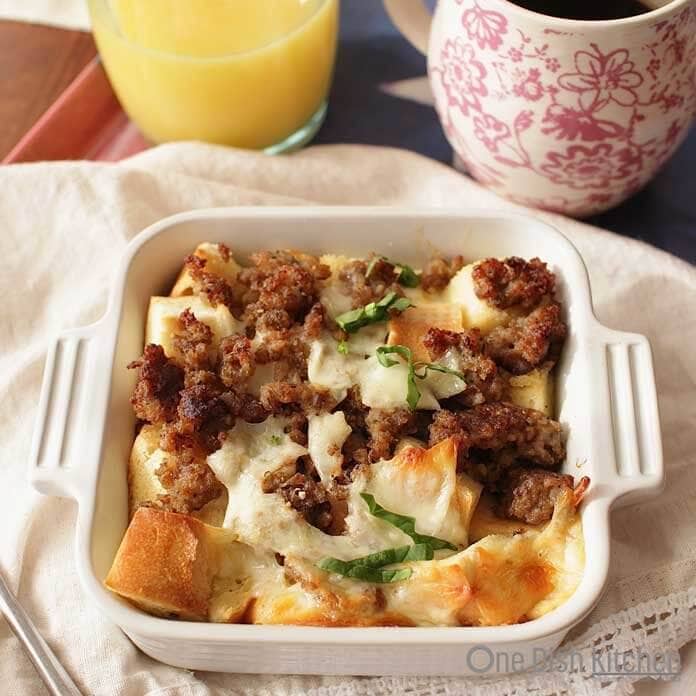 Breakfast casserole in a small baking dish next to a glass of orange juice and a coffee mug