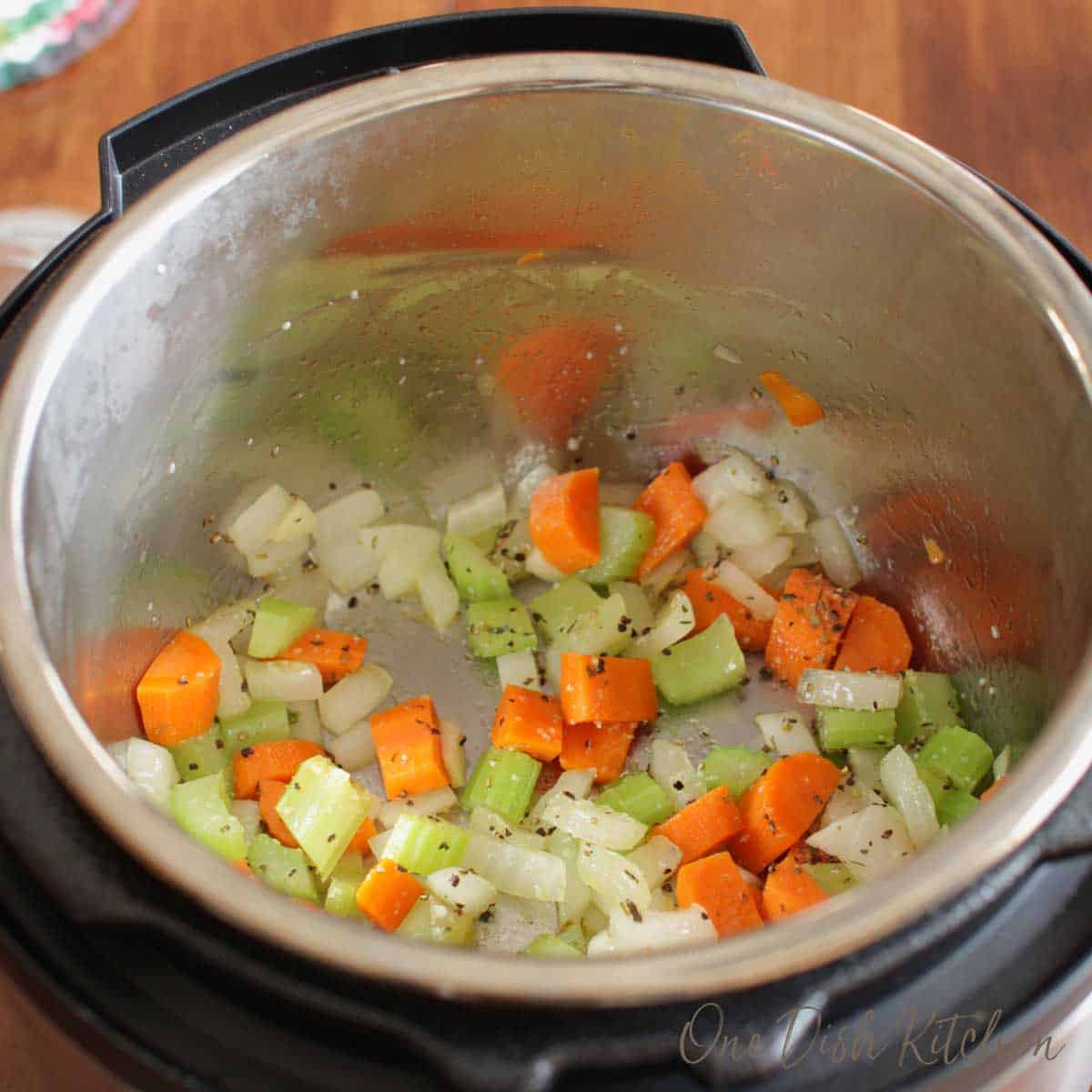 Carrots, onions, and celery cooking in an instant pot for chicken noodle soup