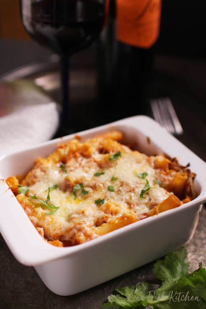 A bowl of baked ziti topped with melted mozzarella cheese and garnished with parsley | one dish kitchen
