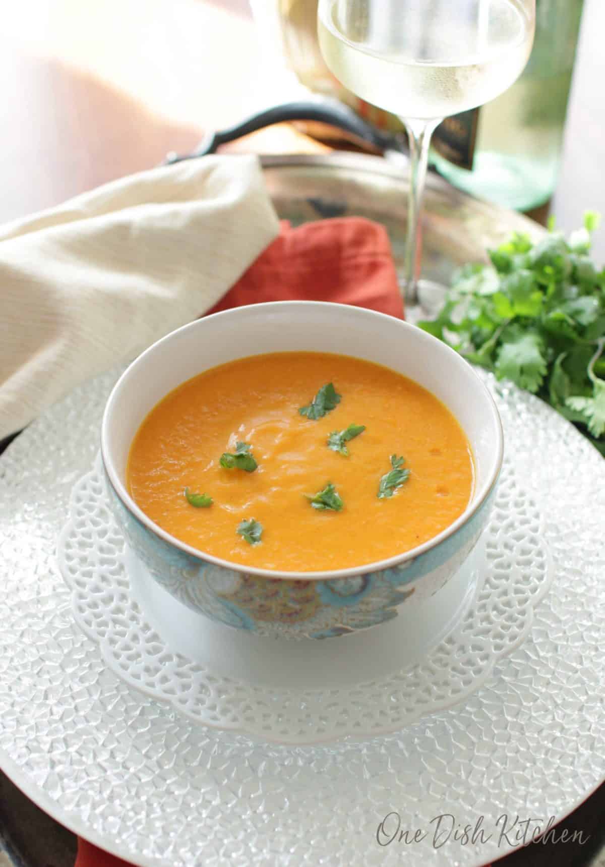 a bowl of carrot soup on a tray next to a glass of white wine.