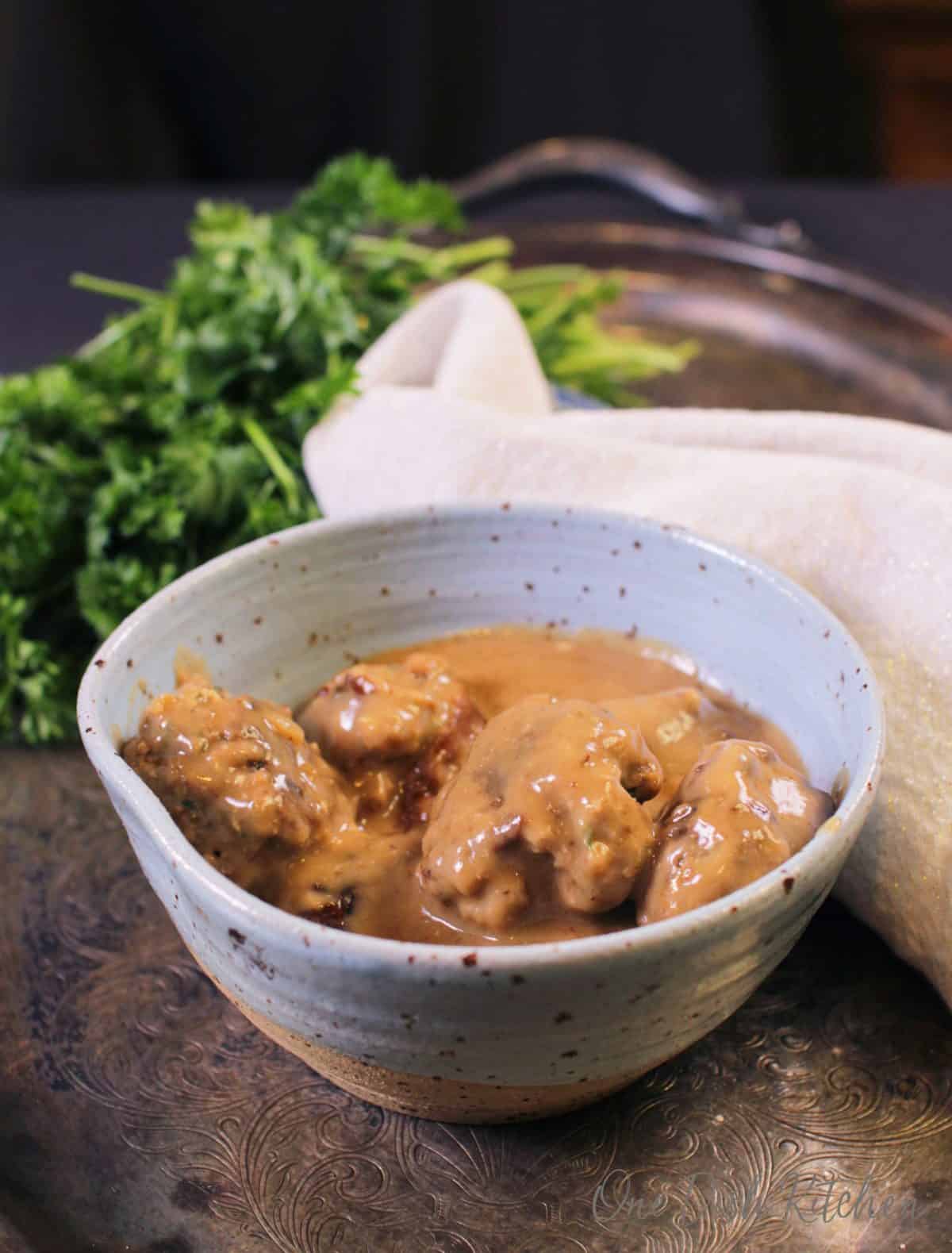 a bowl of swedish meatballs on a tray next to a bunch of parsley.