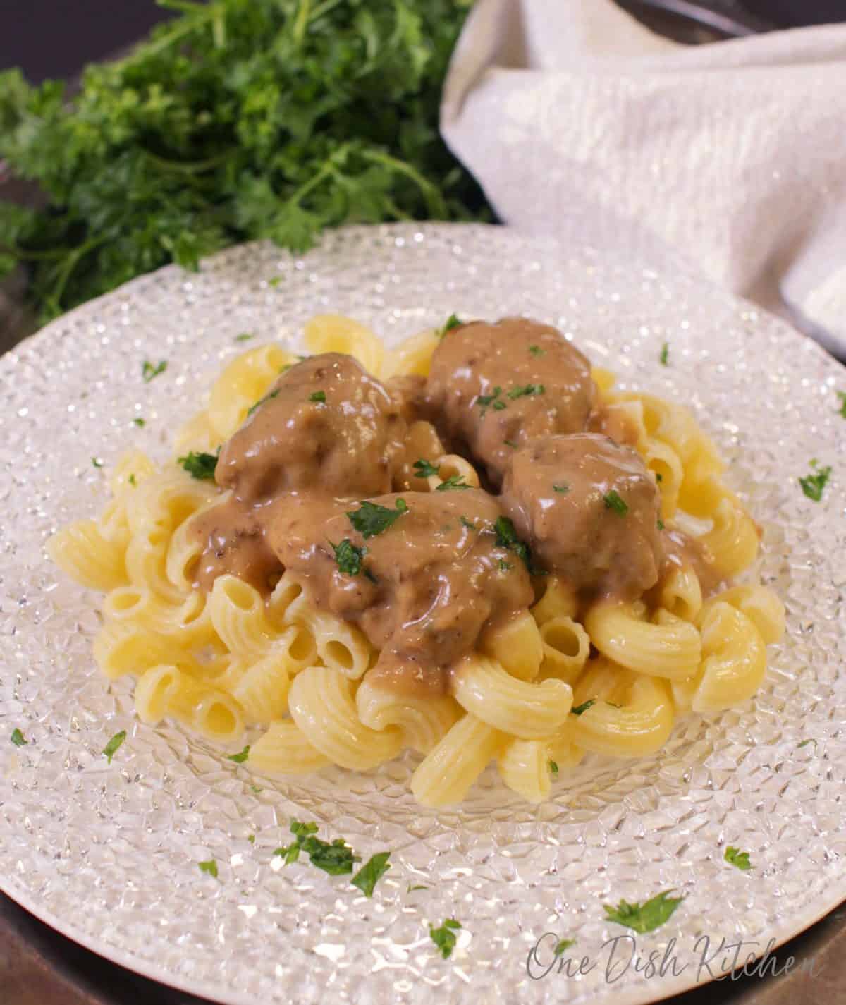 a plate of buttered noodles with swedish meatballs and gravy spooned on top.