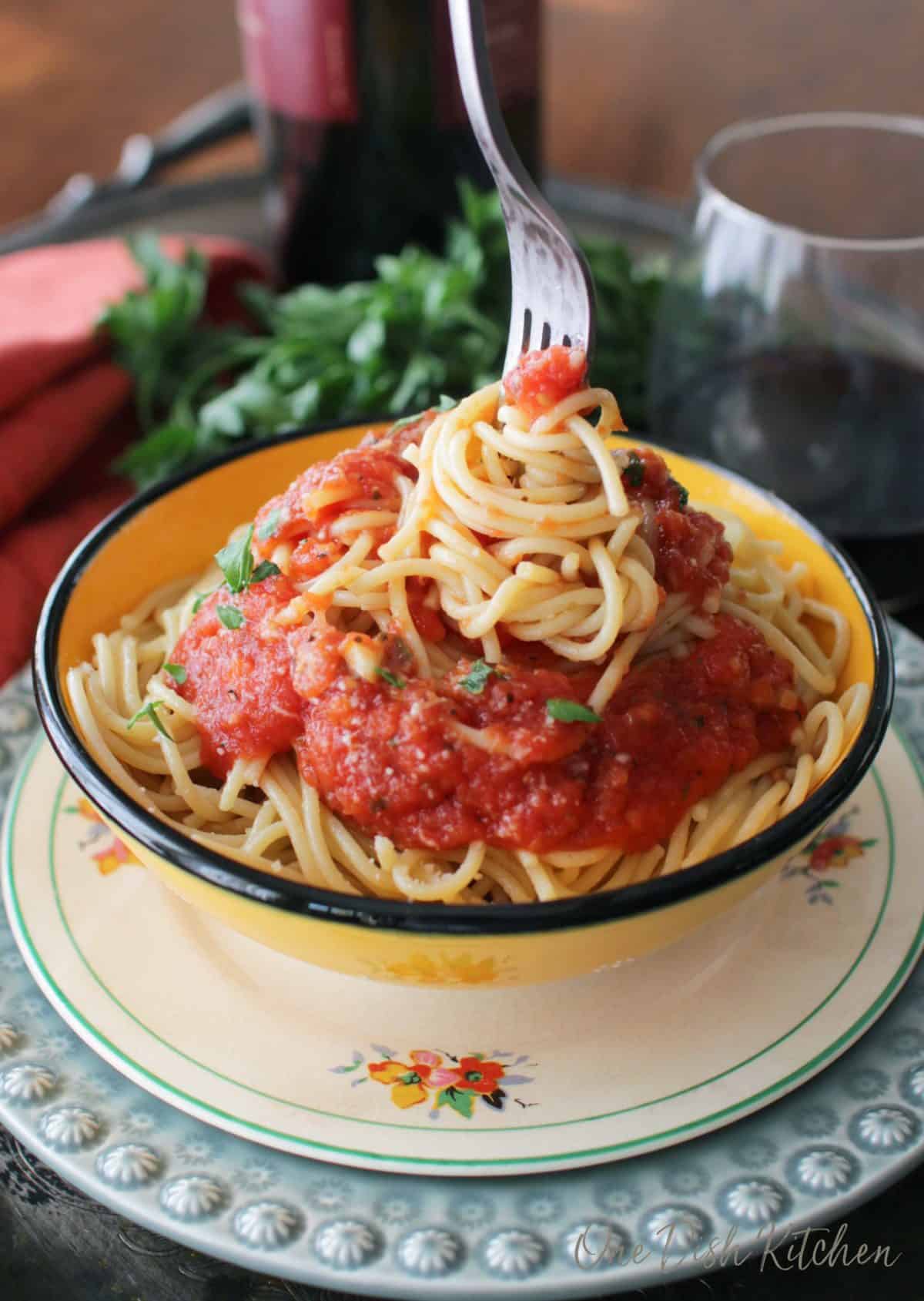 A fork swirling spaghetti that is topped with tomato sauce on a metal tray with a glass of red wine