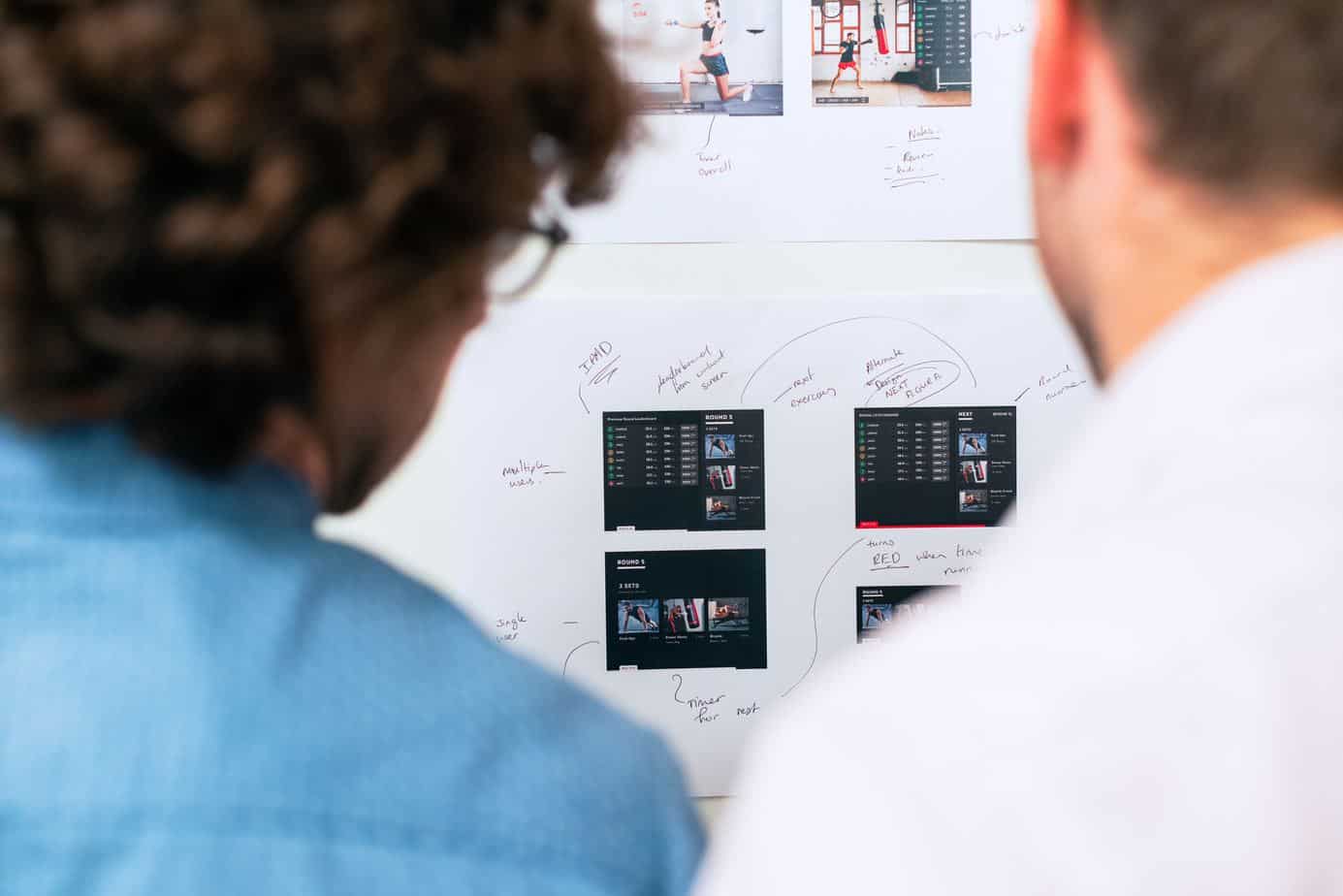 Two designers looking at whiteboard with design mockups.