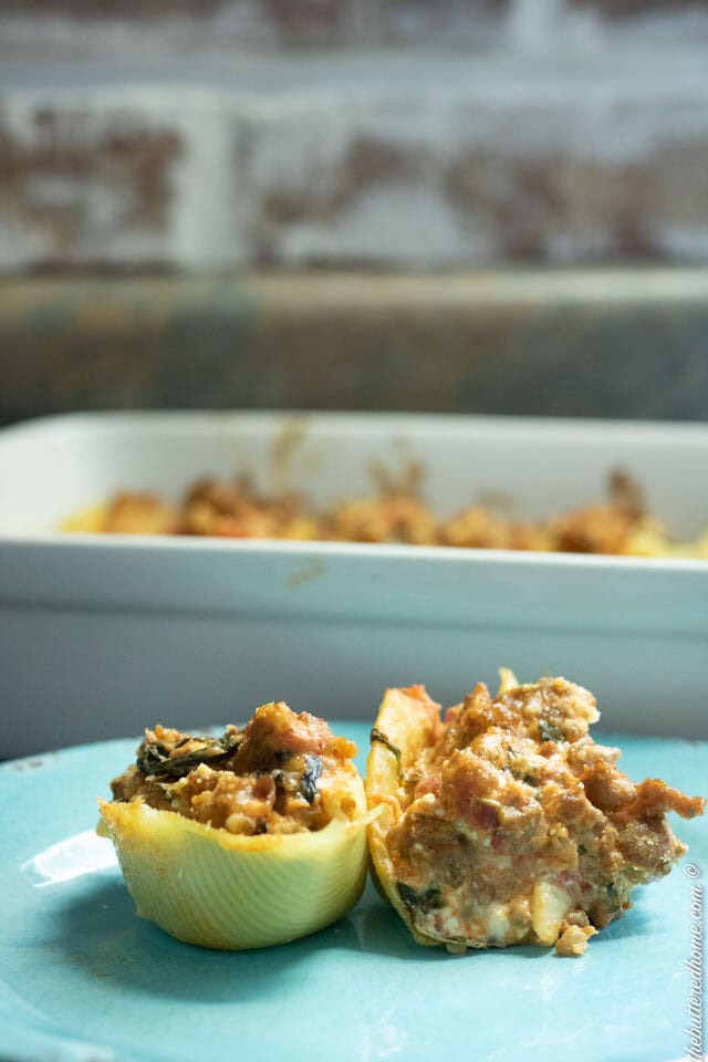 sausage and spinach stuffed shells on a blue plate with entire pan in background