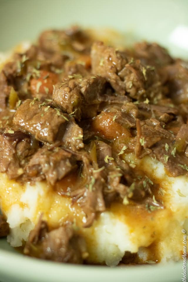 close up of smoother beef tips on bed of mashed potatoes in a green bowl