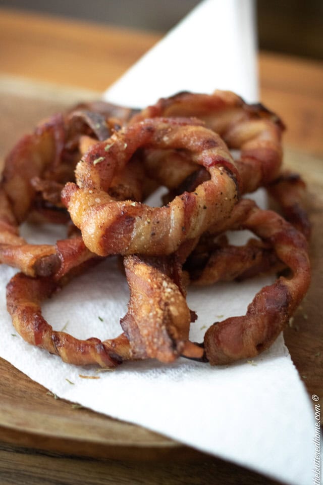 a stack of bacon wrapped onion rings on a white napkin sprinkled with parsley