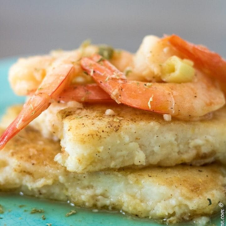 two grit cakes stacked on a blue plate with cooked shrimp on top