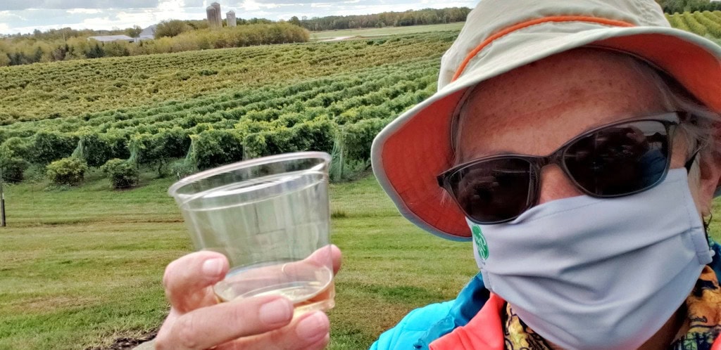 unstoppable stacey in mask holds wine glass with green Parallel 44 winery vineyards behind