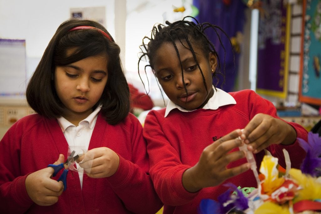 Two schoolchildren are immersed in making something with scissors and card