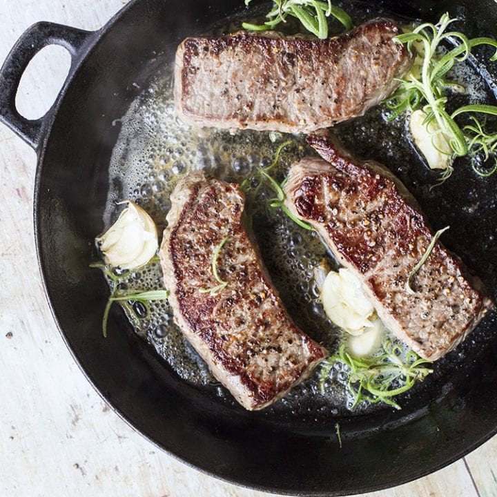 3 striploin steaks in a cast iron skillet with rosemary and garlic.