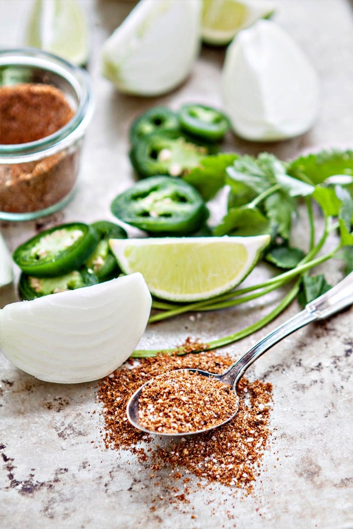 onion, lime, and cilantro on a sheet pan with spoon of seasoning