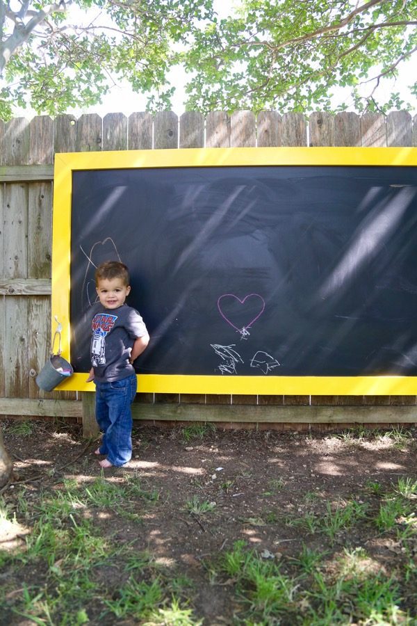 toddler posing in front of a chalkboard hanging on fence