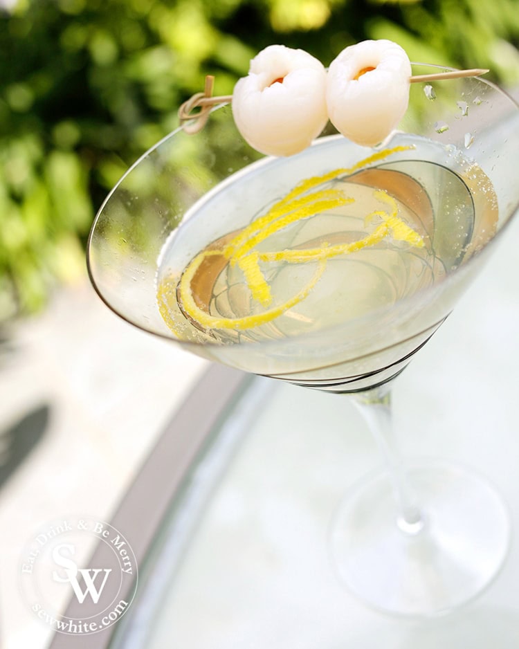 Freshly served up Lemon Lychee Martini in a large glass martini glass with strips of lemon inside and decorated with lychees.